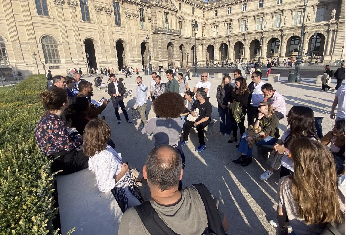 Groupe de collaborateurs en équipe explorant les galeries du musée du Louvre lors d'un rallye team building, roadbook en main