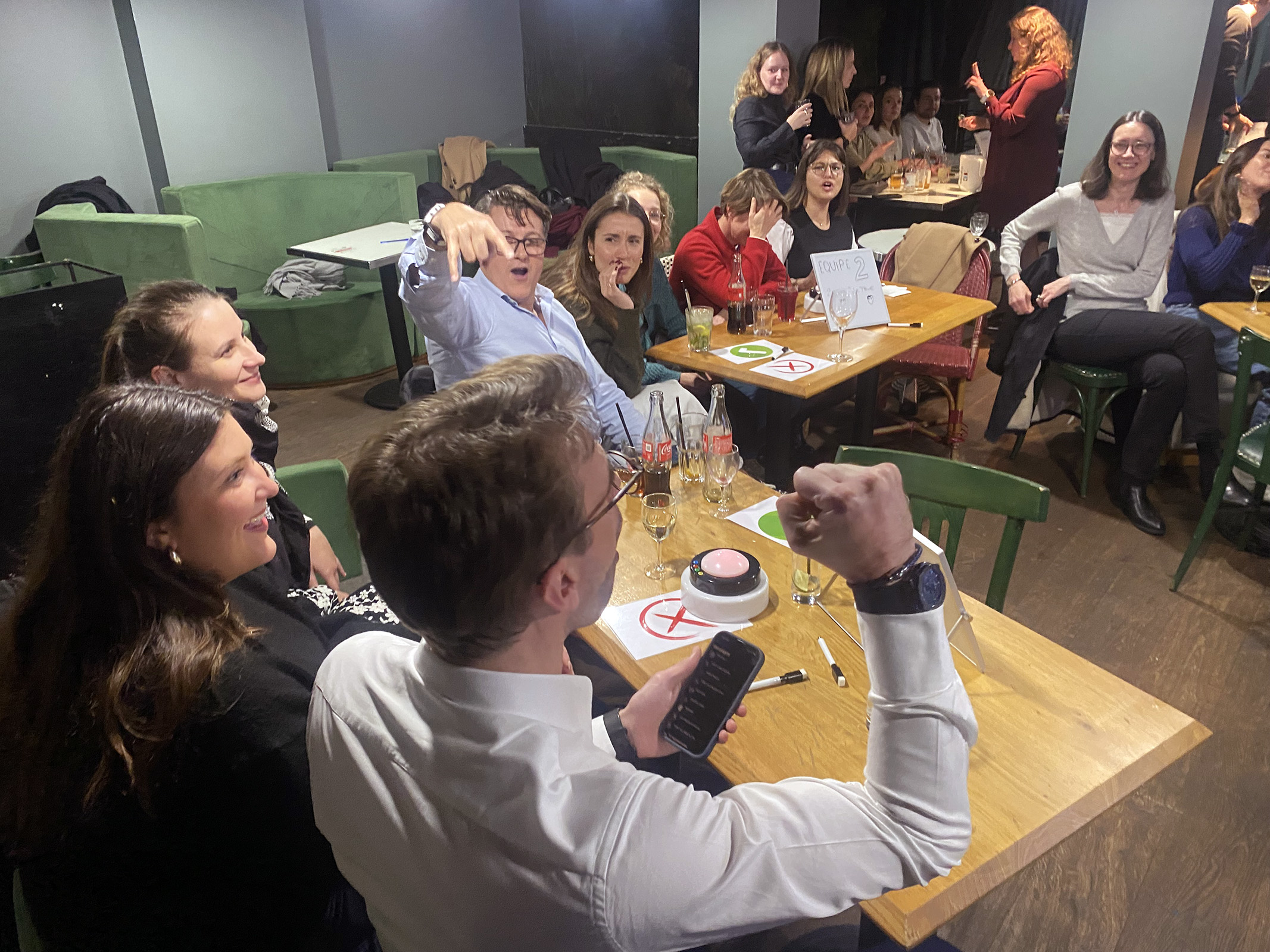 Équipe d'entreprise en pleine animation Grand Quiz team building, animateur professionnel au micro devant plusieurs tables, ambiance soirée festive