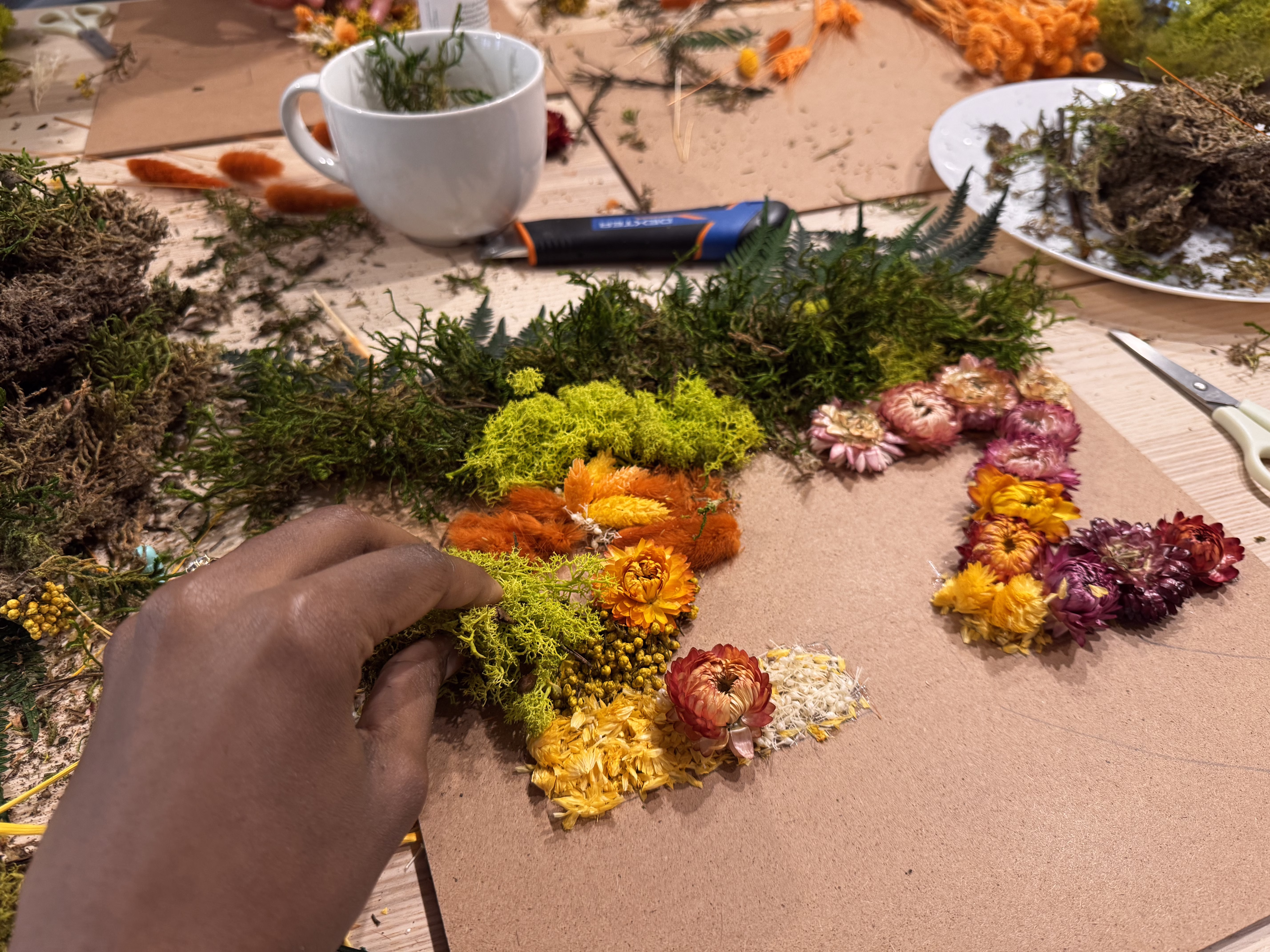 Participants d'un atelier végétal en entreprise, assemblant des mousses et fleurs séchées sur leurs pièces de puzzle, ambiance apaisée et créative