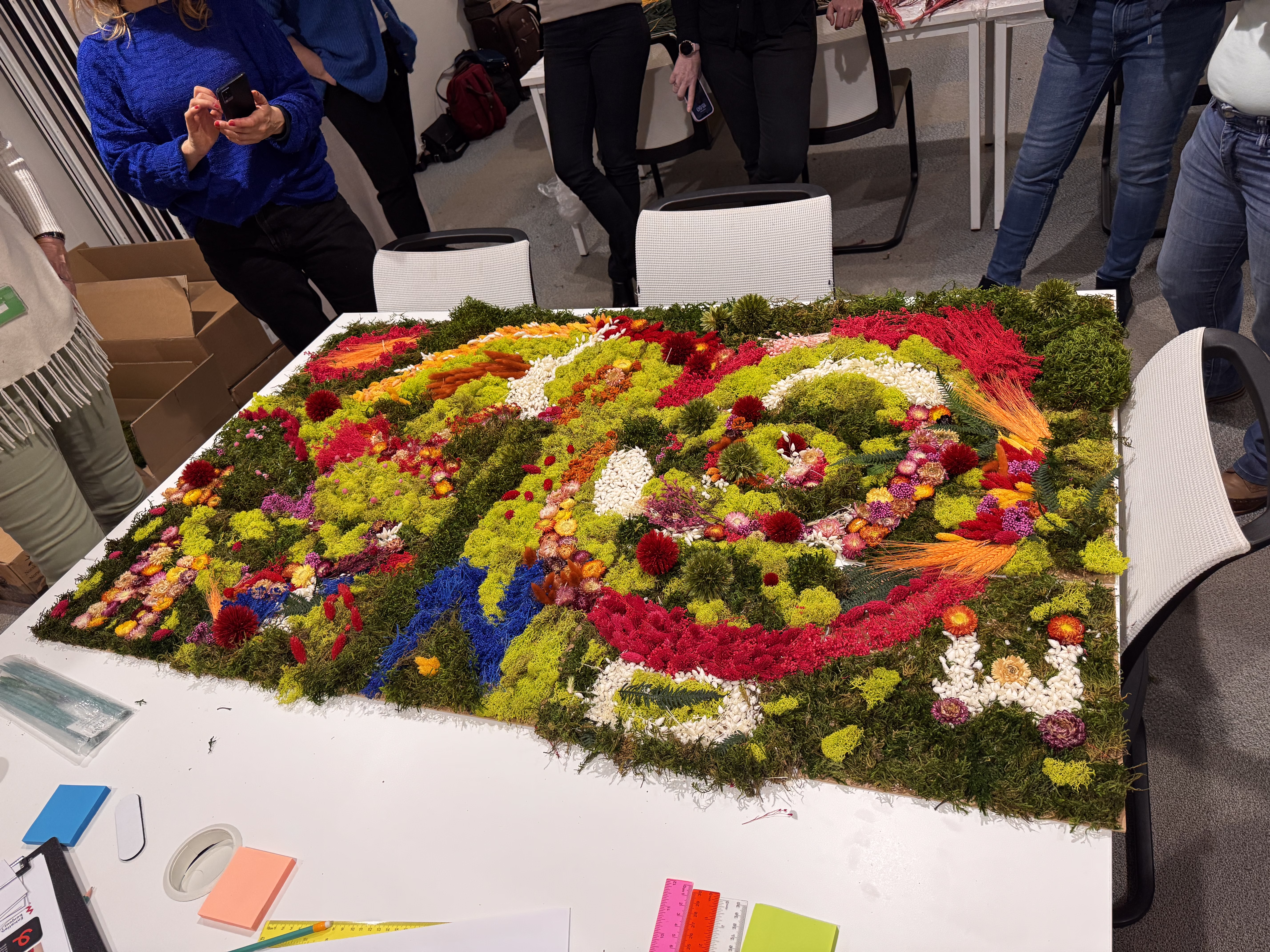 Participants en atelier puzzle végétal, créant chacun leur pièce avec mousses et fleurs séchées dans un cadre calme et collaboratif